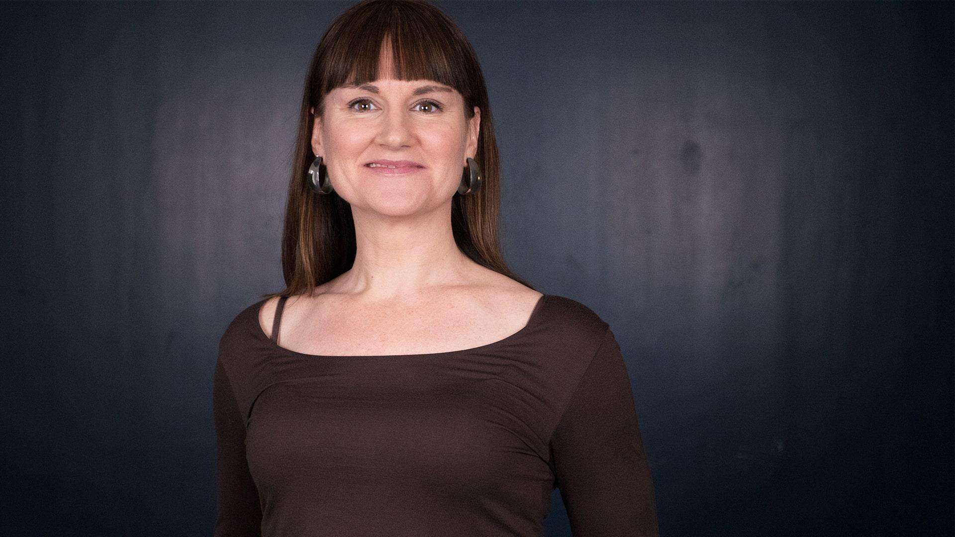 Sofia Niklasson, Radiokören. Kvinna i långt mörkt hår och lugg tittar rakt in i kameran och ler. Hon har stora örhängen och är klädd i en båtringad brun topp.