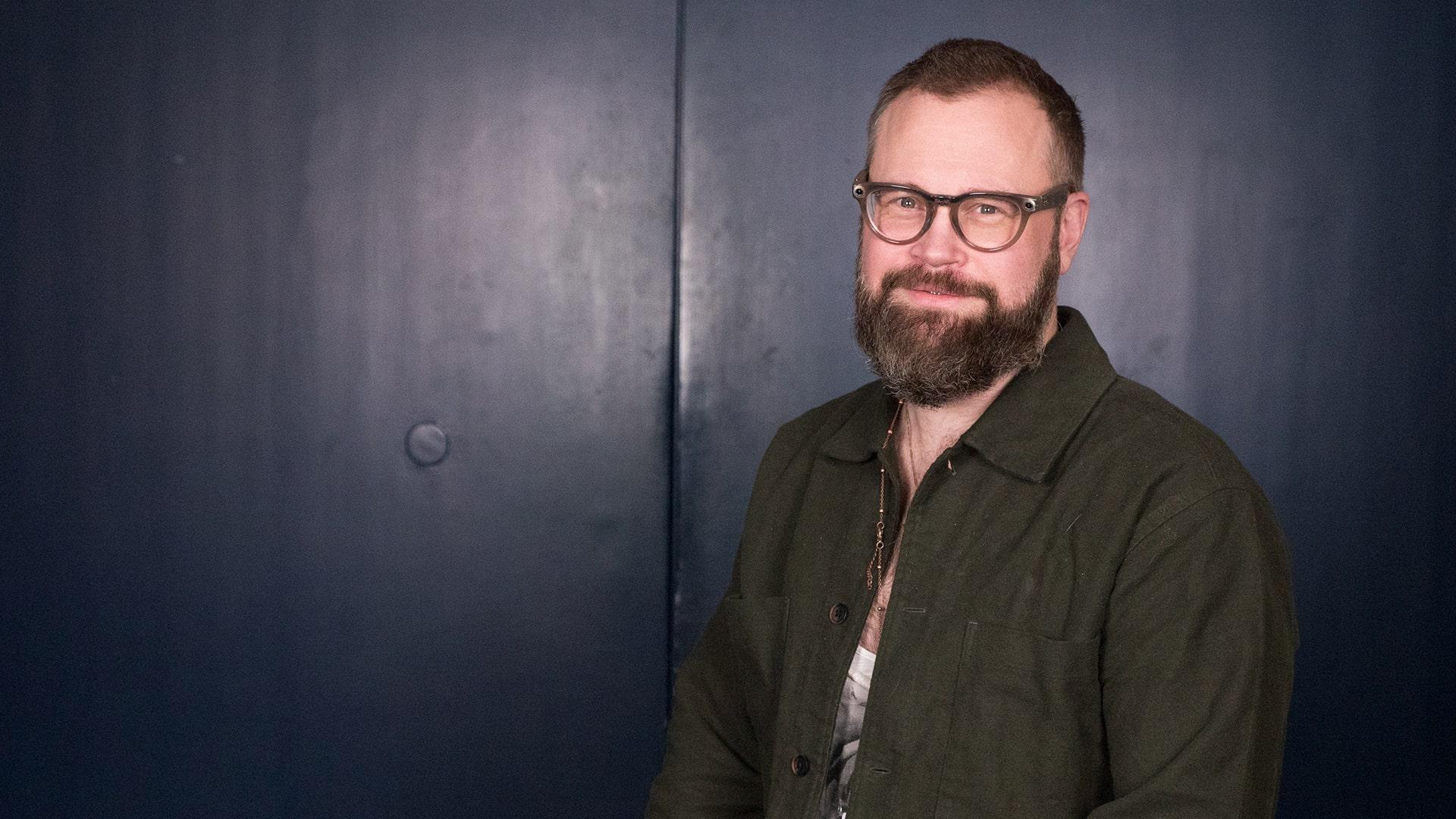 Love Tronner, Radiokören. Närbild på leende man med glasögon och mörkt skähgg. Klädd i mörkt grön skjorta.