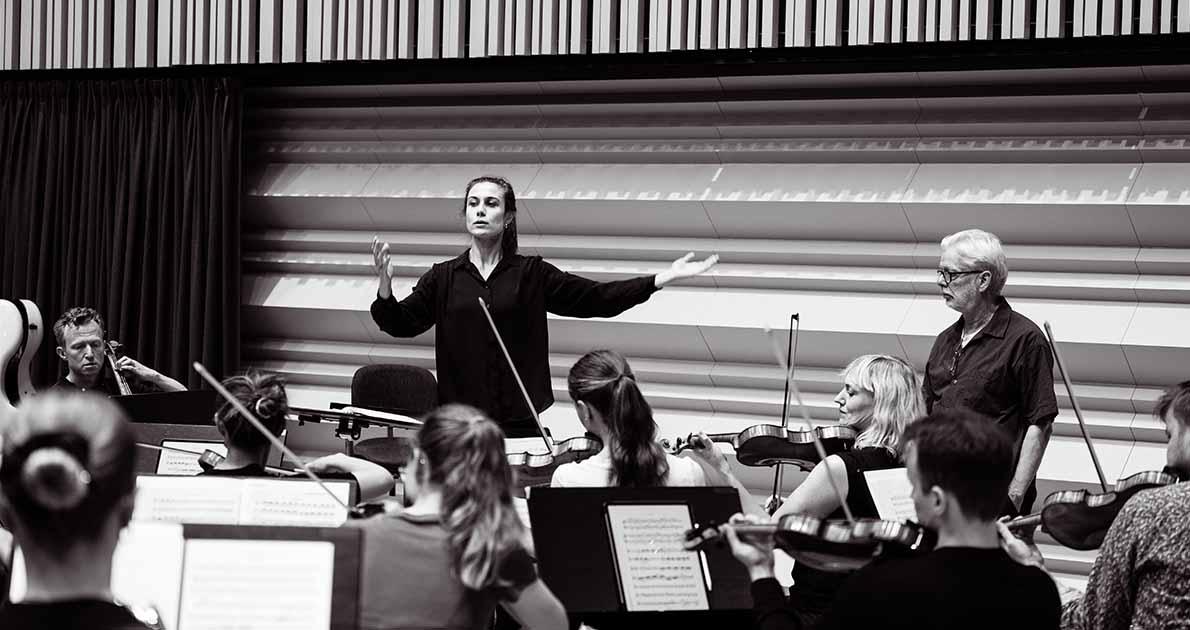 En ung, kvinnlig dirigent dirigerar en orkester