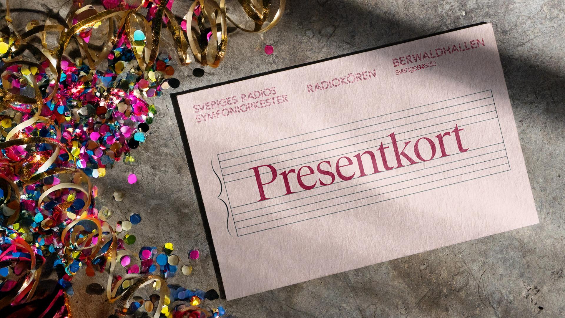 Ett rosa presentkort ligger på betong. Till vänster om kortet ligger glitterconfetti och girlanger.